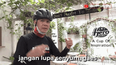 A Man Wearing A Helmet And A Mask Stands In Front Of A Sign That Says Hero Coffee GIF