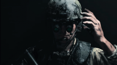 A Man Wearing A Helmet And A Microphone Holds A Gun In His Hand GIF