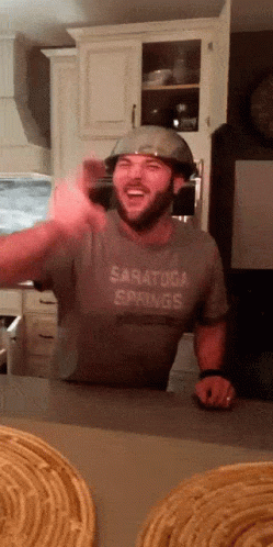 A Man Wearing A Helmet And A Saratoga Springs Shirt Laughs GIF