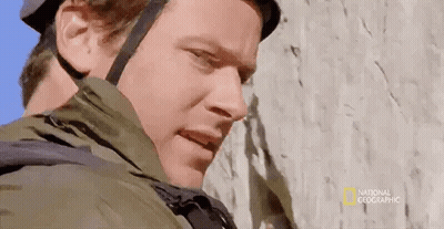 A Man Wearing A Helmet And Jacket Is Standing Next To A Rock Wall . GIF