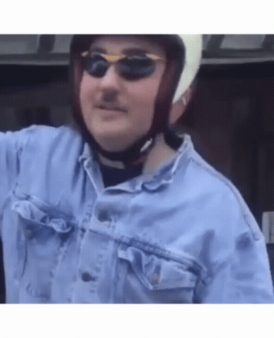 A Man Wearing A Helmet And Sunglasses Is Standing In A Car . GIF