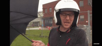 A Man Wearing A Helmet Is Holding An Umbrella In Front Of A Building GIF