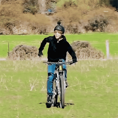 A Man Wearing A Helmet Is Riding A Bike On A Grassy Field GIF