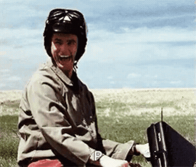 A Man Wearing A Helmet Is Sitting In A Field Holding A Briefcase With The Letter P On It GIF