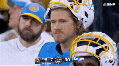 A Man Wearing A Helmet Sits In The Stands Watching A Football Game GIF
