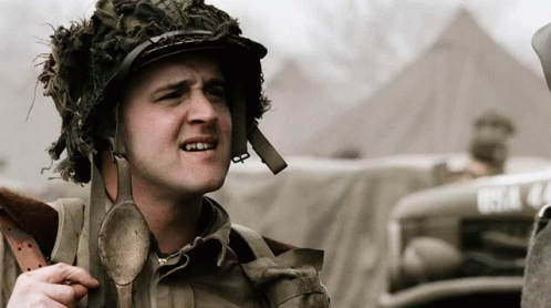 A Man Wearing A Helmet With A Spoon Around His Neck Is Standing In Front Of A Vehicle With The License Plate Bsa 44 GIF