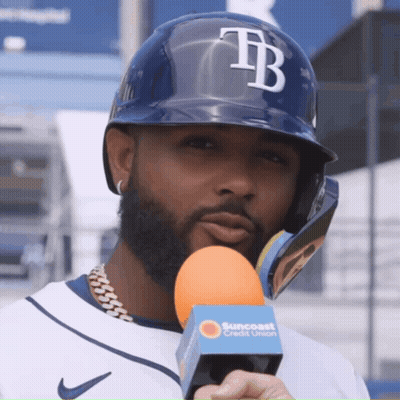 A Man Wearing A Helmet With The Letter Tb On It Holds An Orange Microphone GIF