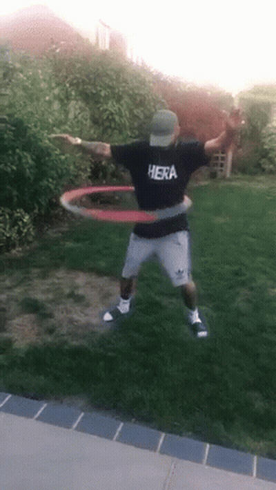 A Man Wearing A Hera Shirt Is Playing With A Hula Hoop In A Yard . GIF