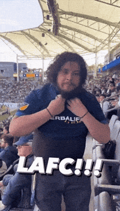 A Man Wearing A Herbalife Shirt Is Standing In A Crowded Stadium GIF