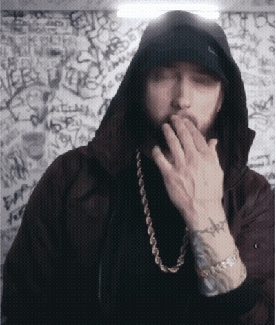A Man Wearing A Hooded Jacket And A Gold Chain Covering His Mouth GIF
