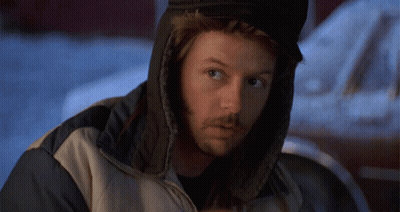 A Man Wearing A Hooded Jacket And Ear Warmers Looks At The Camera GIF