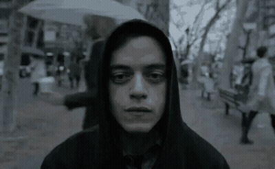 A Man Wearing A Hooded Jacket And Tie Is Standing On A Sidewalk In The Rain . GIF