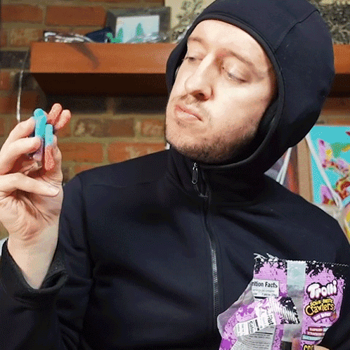A Man Wearing A Hooded Jacket Is Holding A Bag Of Toon Candy In His Hands GIF