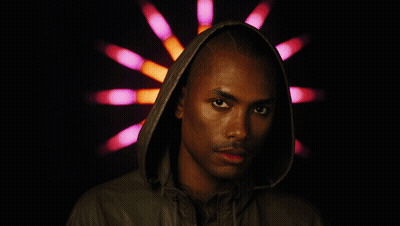A Man Wearing A Hooded Jacket Stands In Front Of A Pink And Orange Light GIF