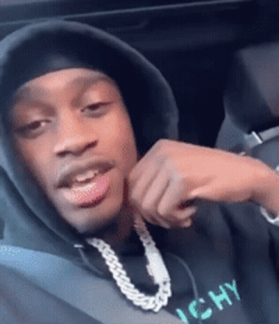 A Man Wearing A Hooded Sweatshirt And A Chain Around His Neck Is Sitting In A Car . GIF