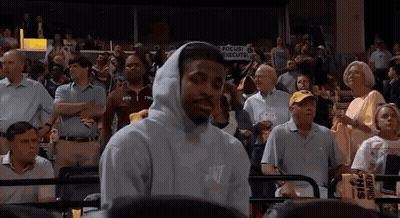 A Man Wearing A Hooded Sweatshirt Is Standing In Front Of A Crowd Of People At A Basketball Game . GIF
