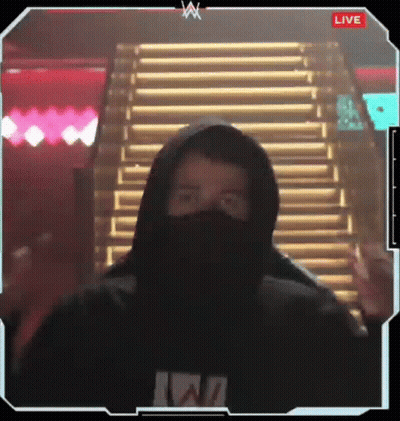 A Man Wearing A Hoodie And A Mask Is Standing In Front Of Stairs And Giving A Peace Sign . GIF