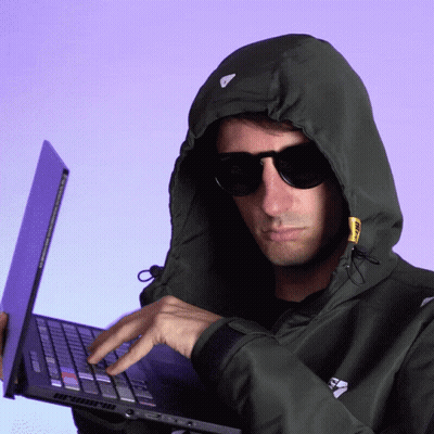 A Man Wearing A Hoodie And Sunglasses Is Typing On His Laptop GIF
