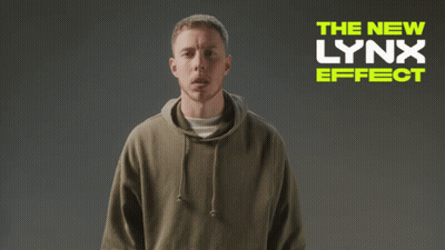 A Man Wearing A Hoodie Is Standing In Front Of A Sign That Says The New Lynx Effect GIF