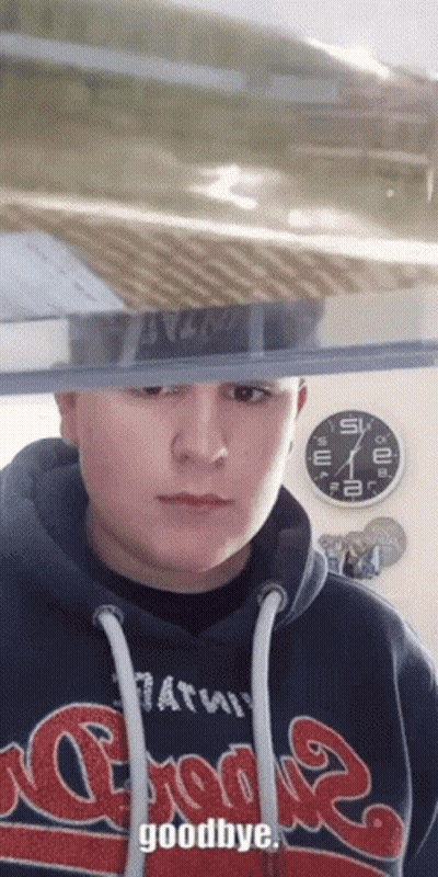A Man Wearing A Hoodie That Says Goodbye Stands In Front Of A Clock GIF