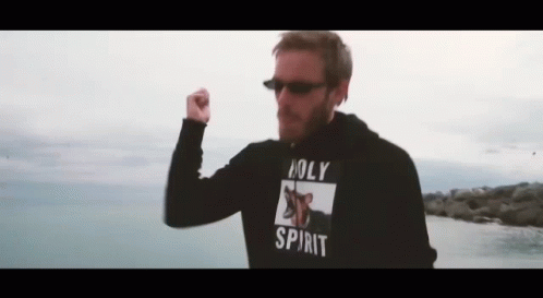 A Man Wearing A Hoodie That Says Holy Spirit Is Standing In Front Of The Ocean . GIF