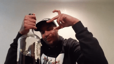 A Man Wearing A Hoodie That Says ' Nike ' On It Is Opening A Bottle GIF