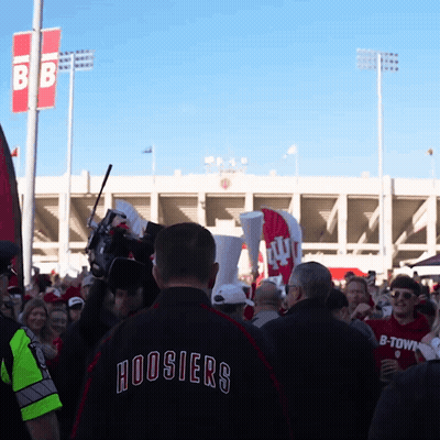 A Man Wearing A Hoosier 'S Jacket Stands In A Crowd Of People GIF