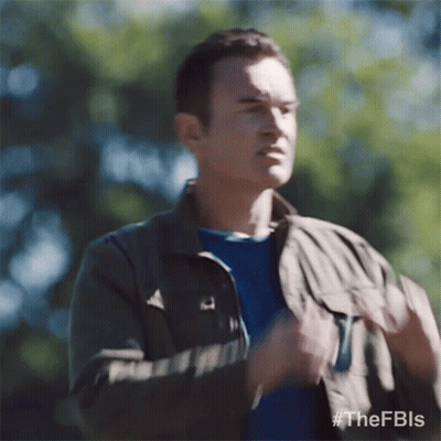 A Man Wearing A Jacket And A Blue Shirt Is Standing In The Woods And Making A Funny Face . GIF