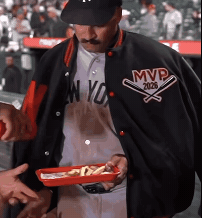 A Man Wearing A Jacket That Says Mvp 2026 Holds A Tray Of Food GIF