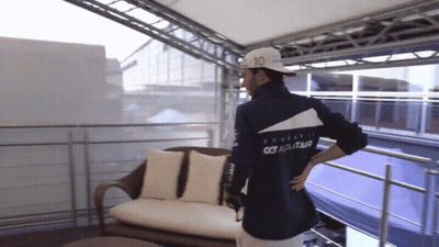 A Man Wearing A Jacket That Says Scuderia On The Back Is Standing On A Balcony GIF
