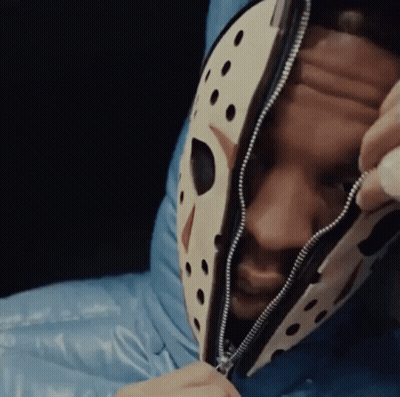 A Man Wearing A Jason Voorhees Mask Is Laying In A Blue Sleeping Bag . GIF