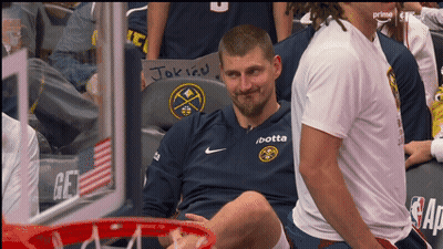 A Man Wearing A Jersey That Says / Botta Sits In A Basketball Hoop GIF
