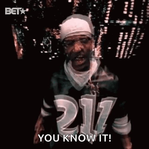 A Man Wearing A Jersey With The Number 211 On It Is Standing In Front Of A City Skyline At Night . GIF