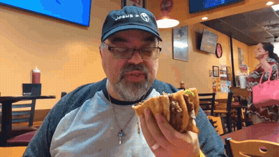 A Man Wearing A Jesus Hat Is Eating A Hamburger GIF