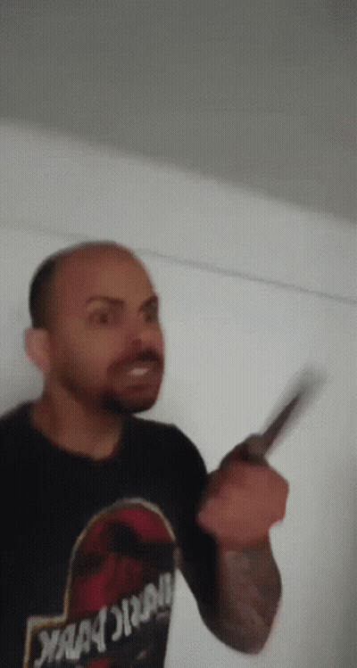 A Man Wearing A Jurassic Park Shirt Is Holding A Knife In His Hand . GIF
