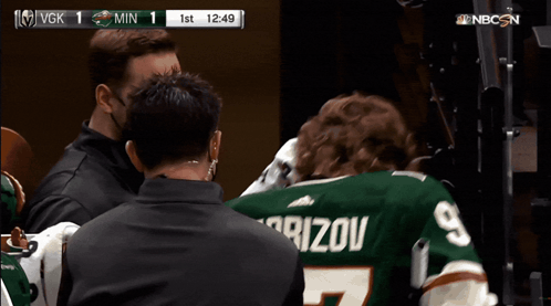 A Man Wearing A Kaprizov Jersey Is Being Escorted By A Man Wearing A Mask GIF