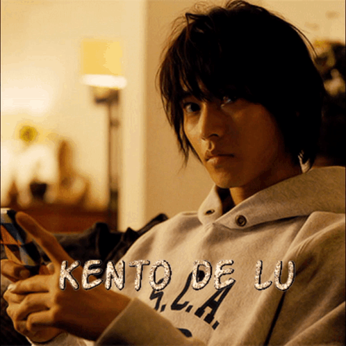 A Man Wearing A Kento De Lu Sweatshirt Is Holding A Cell Phone GIF