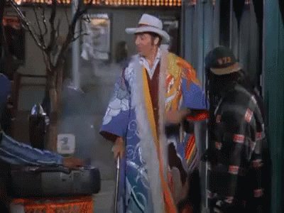 A Man Wearing A Kimono And A Cowboy Hat Is Standing In Front Of A Sign That Says 973 GIF