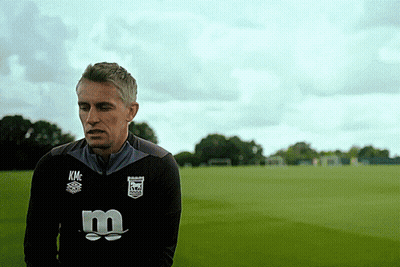 A Man Wearing A Kmc Sweatshirt Stands In A Field GIF