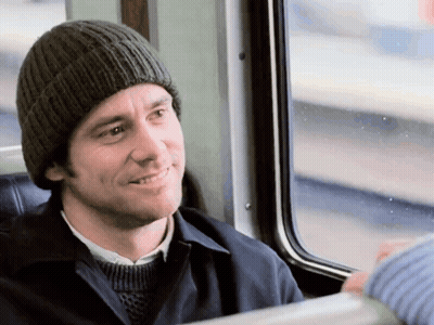 A Man Wearing A Knitted Hat Is Smiling While Sitting On A Train GIF