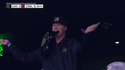 A Man Wearing A La Hat And A Scarf Holds His Fist Up GIF