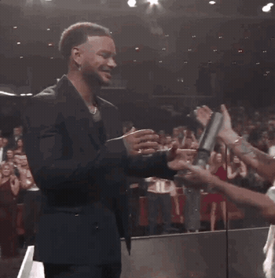 A Man Wearing A La Hat Shakes Hands With Another Man In A Suit GIF
