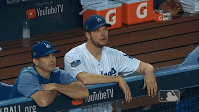 A Man Wearing A La Hat Sits In A Dugout Next To Another Man GIF