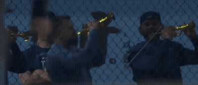 A Man Wearing A La Hat Stands Behind A Chain Link Fence While Another Man Plays A Violin GIF