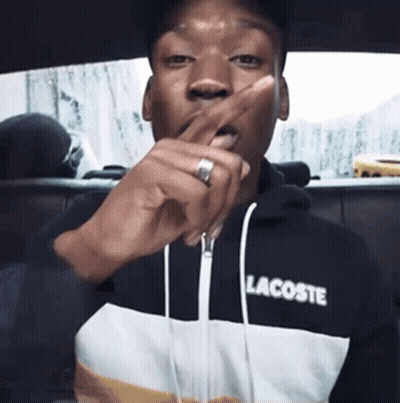 A Man Wearing A Lacoste Sweatshirt Is Covering His Mouth With His Hand GIF