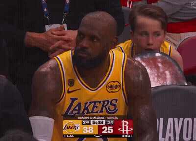 a man wearing a lakers jersey sits in a stadium