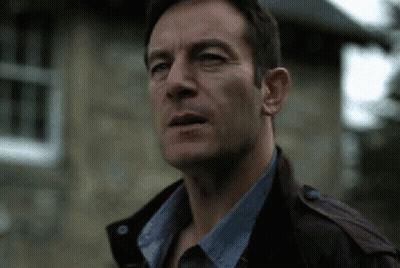A Man Wearing A Leather Jacket And A Blue Shirt Is Standing In Front Of A Stone Building . GIF