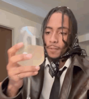 A Man Wearing A Leather Jacket And Tie Is Holding A Spray Bottle . GIF