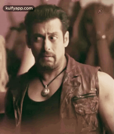 A Man Wearing A Leather Vest And A Necklace Is Standing In Front Of A Crowd Of People . GIF