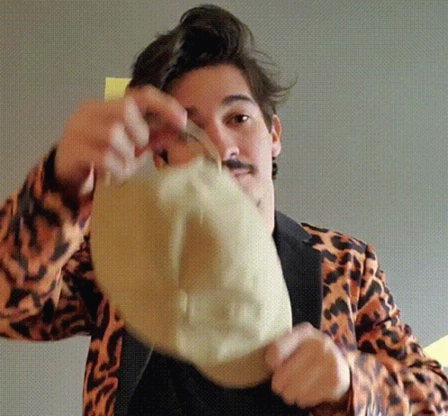 A Man Wearing A Leopard Print Jacket Is Holding A Hat In Front Of His Face GIF